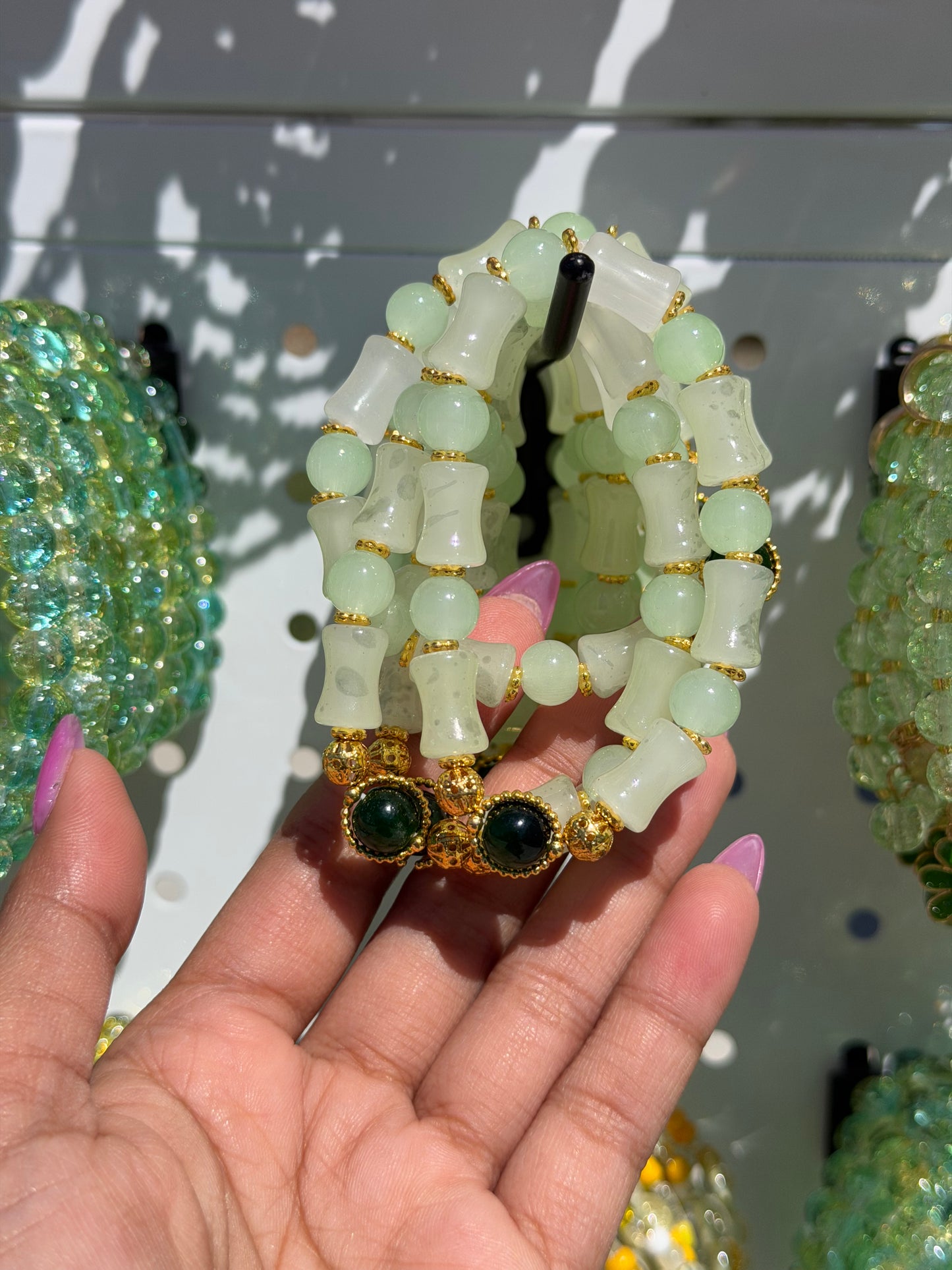Green beaded bracelets held by a hand, showcasing various styles including light green round and bamboo-shaped beads, gold spacers, and dark green cabochons.