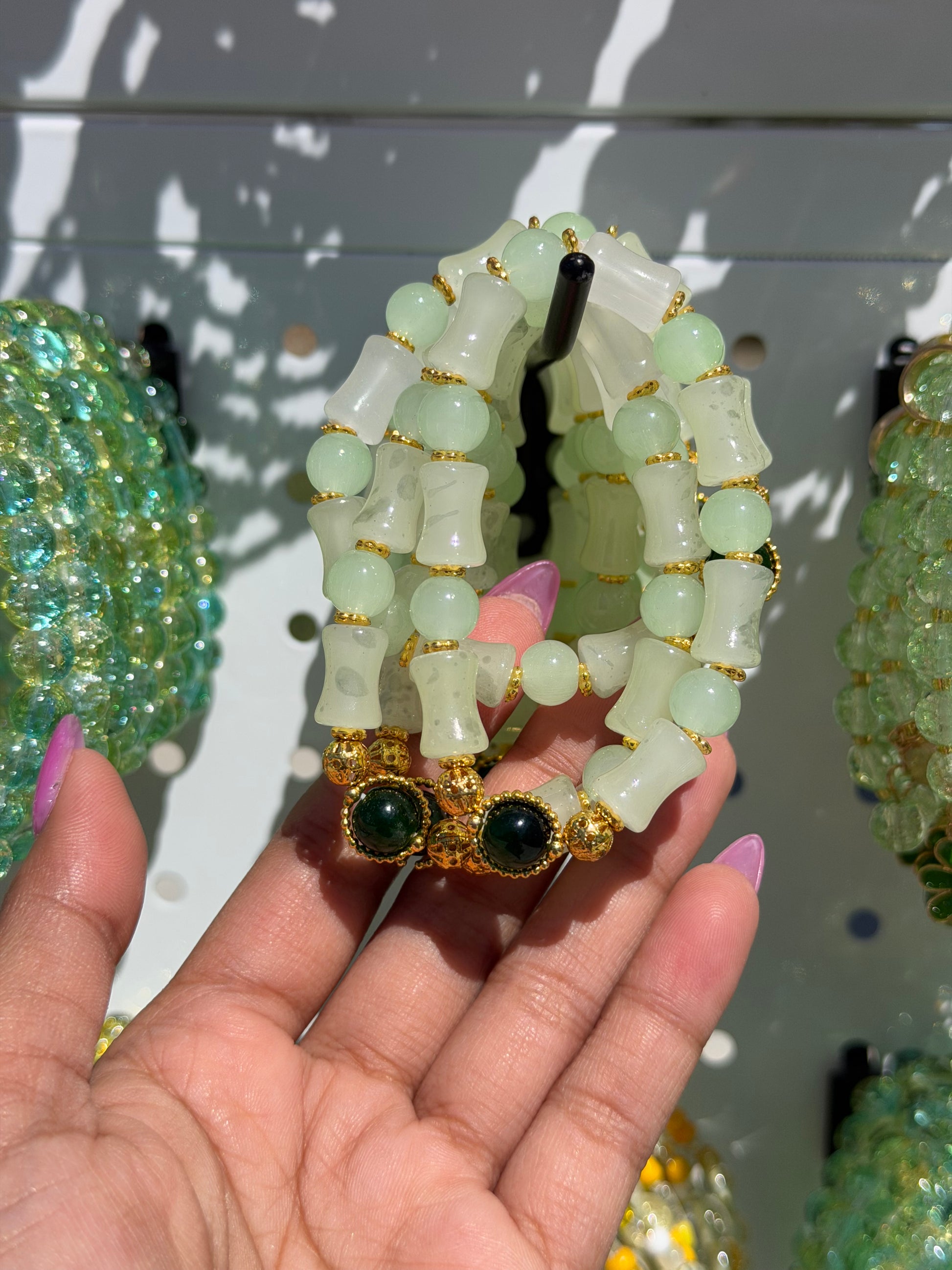 Green beaded bracelets held by a hand, showcasing various styles including light green round and bamboo-shaped beads, gold spacers, and dark green cabochons.