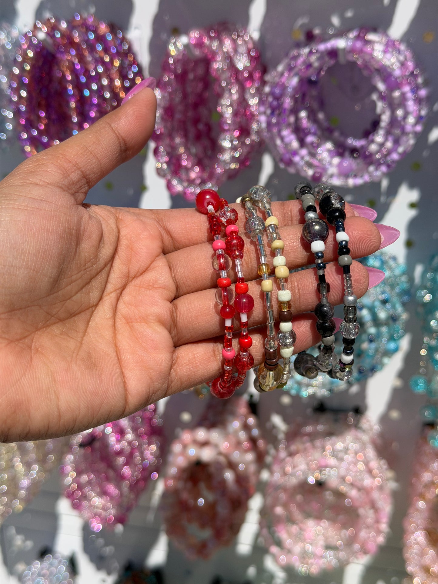 Layered beaded bracelets in red, pink, clear, silver, and black, held by a hand with pink nail polish.