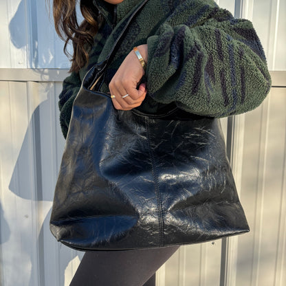 Black tote bag by Quince, with a glossy, crinkled texture and styled with a fuzzy jacket.