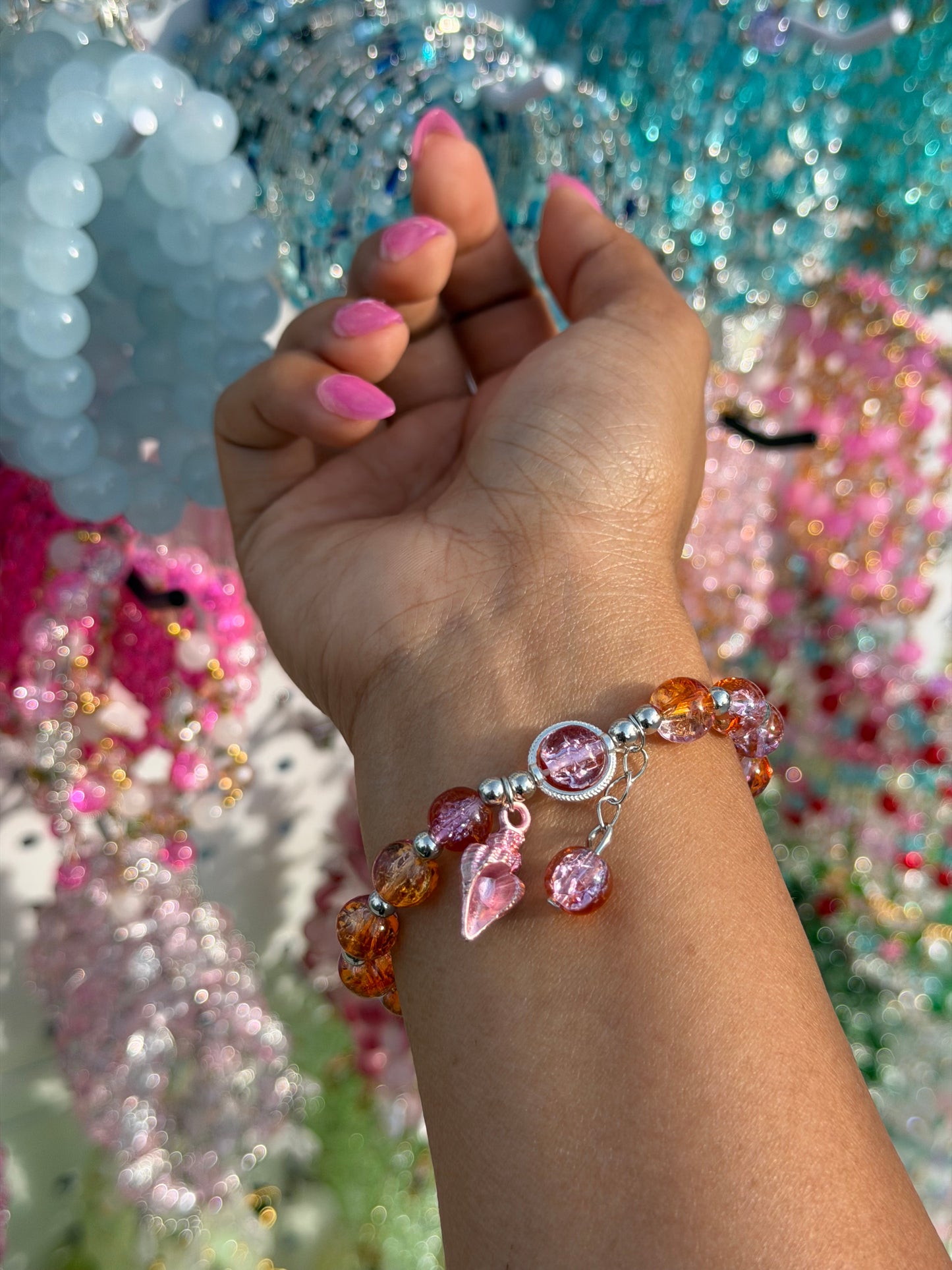 Orange and pink beaded bracelet with a pink seashell charm and round pink charm, worn on a wrist.