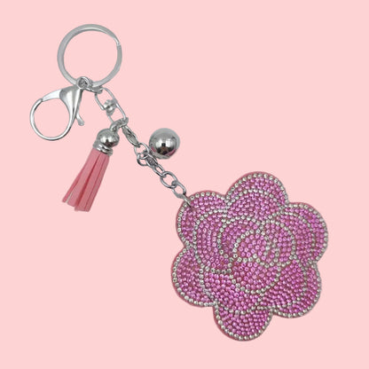 Pink rose-shaped rhinestone keychain with silver hardware on a red background.