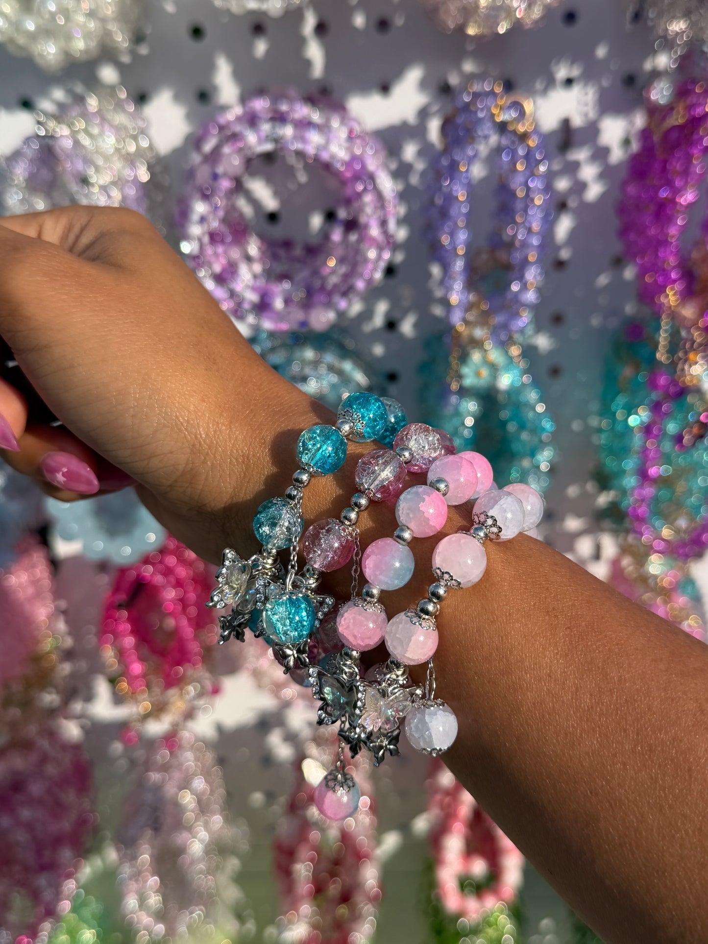 Multicolored beaded bracelets with crackled and ombré blue, pink, white beads, and silver butterfly charms on an arm.