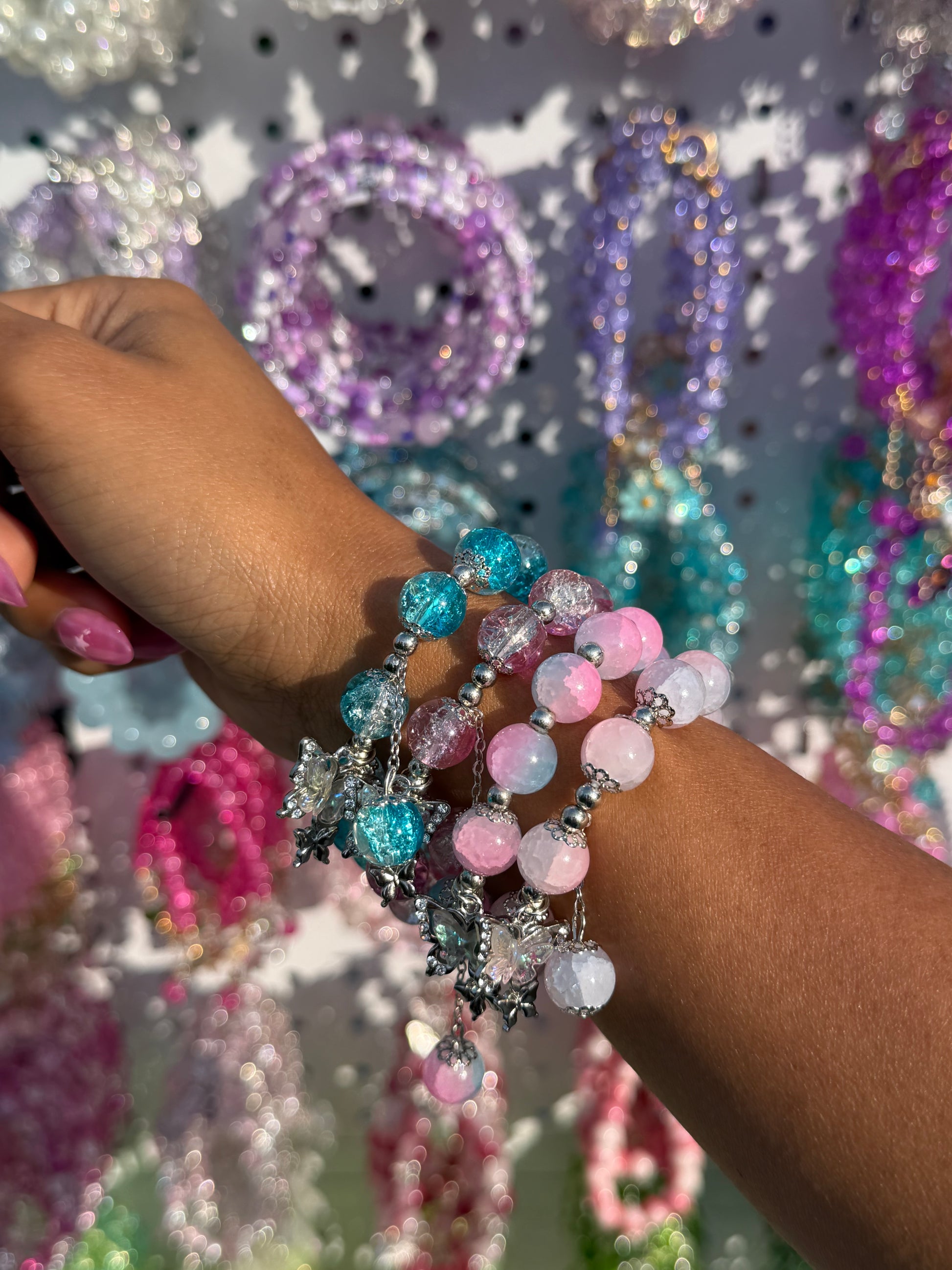 Multicolored beaded bracelets with crackled and ombré blue, pink, white beads, and silver butterfly charms on an arm.