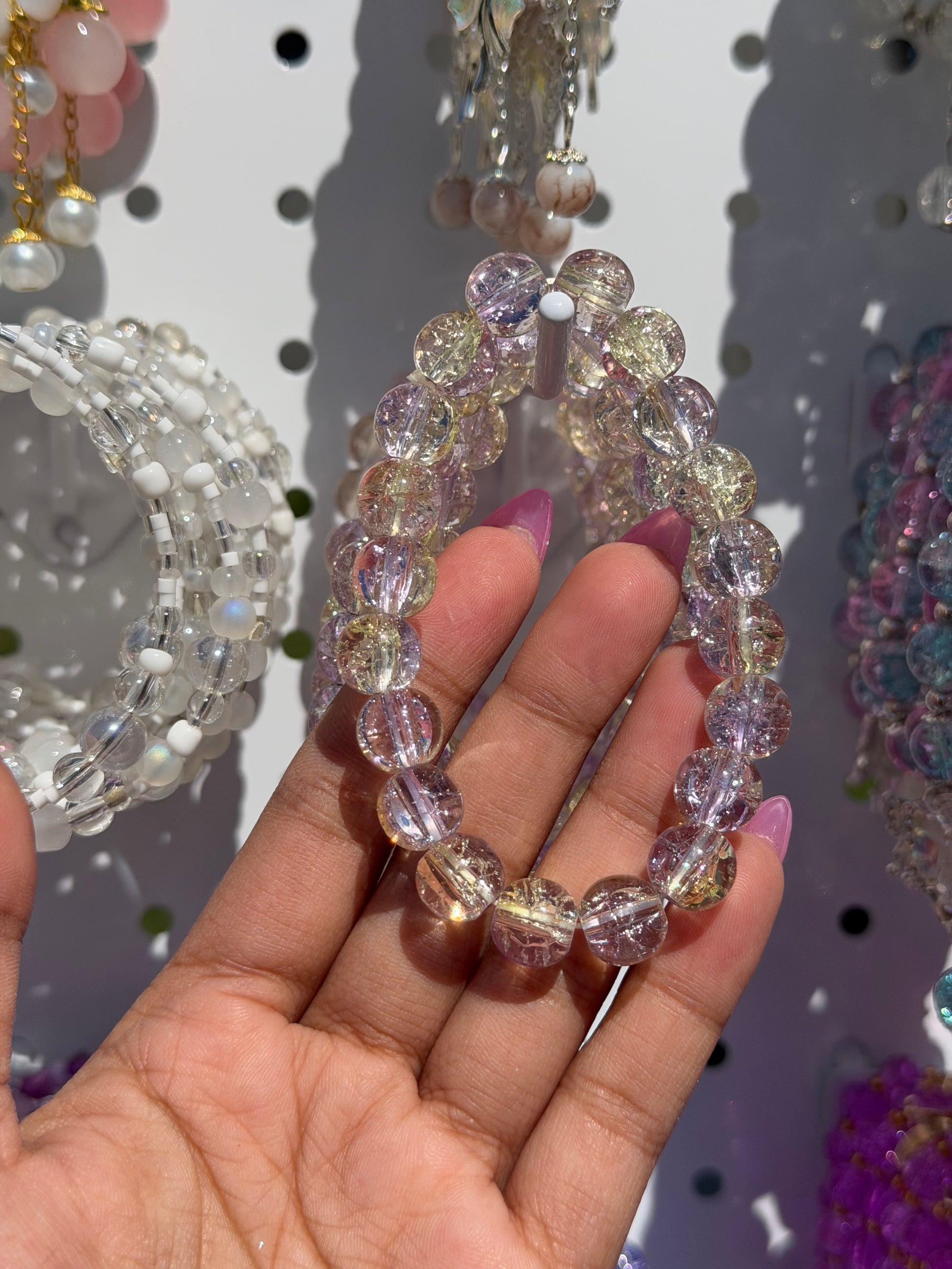 Lilac beaded bracelet with multi-colored cracked glass beads, held by a hand with pink nail polish.