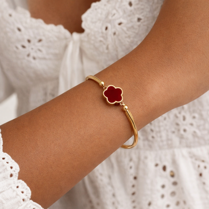Gold-tone Abigail Bracelet with a red four-petal flower charm, worn on an arm against a white lace top.
