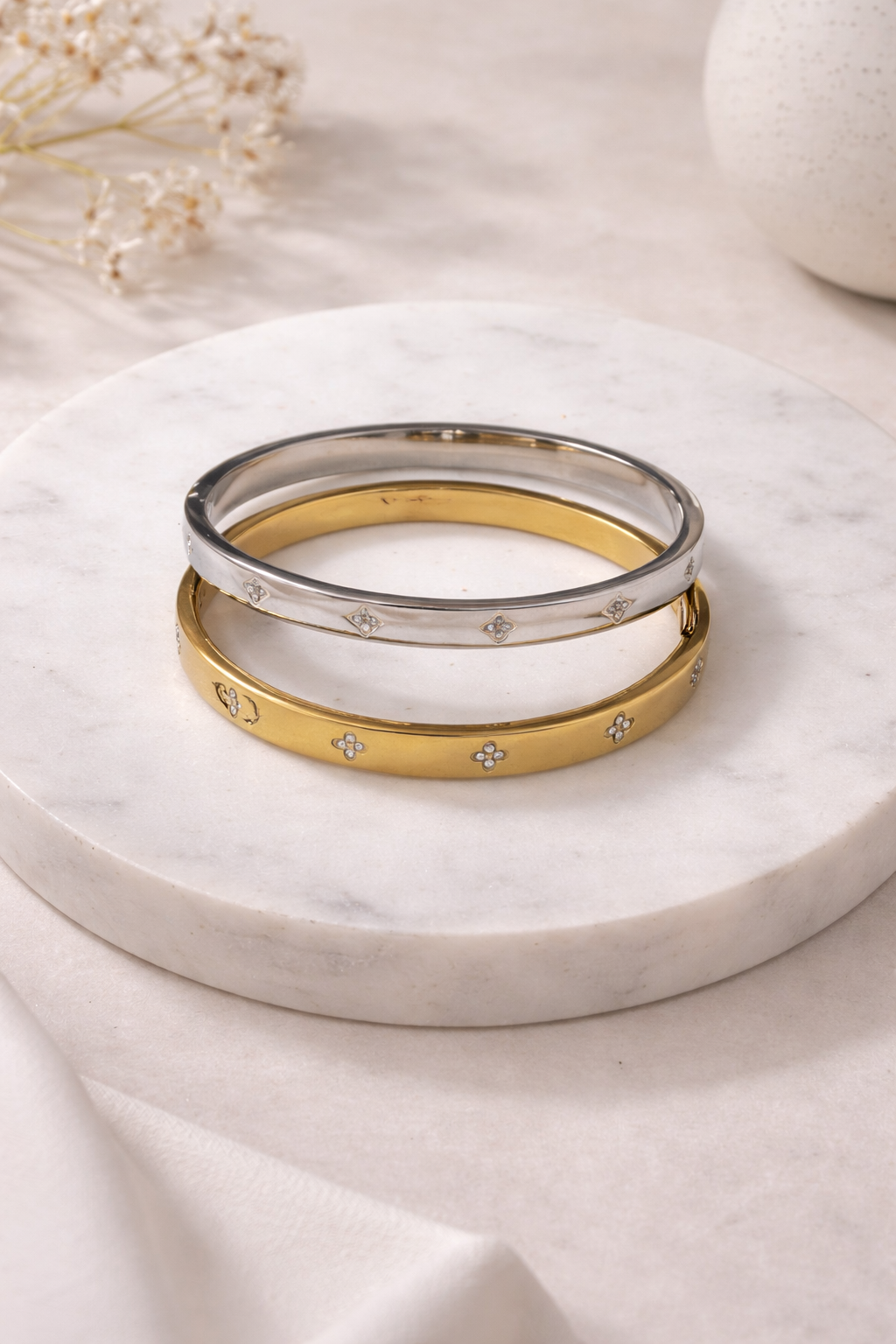 Silver-toned and gold-toned bangles with sparkling quatrefoil patterns, stacked on a marble slab.