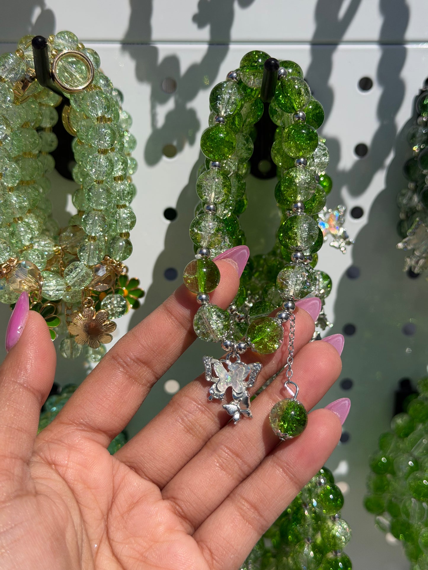 Green beaded bracelets featuring various styles, including shimmering cracked glass beads and butterfly charms, held by a hand.