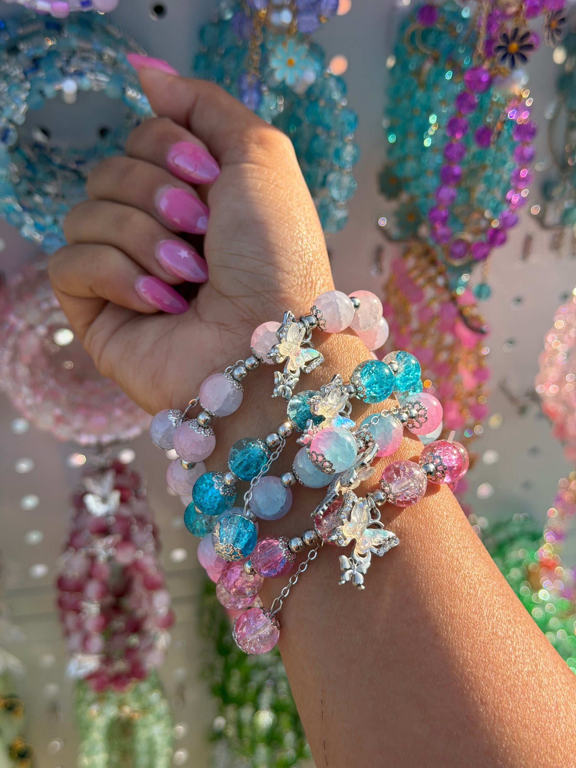Monarch Charm Beaded Bracelet featuring pink, blue, and purple cracked beads with silver butterfly charms, stacked on a hand with pink nails.
