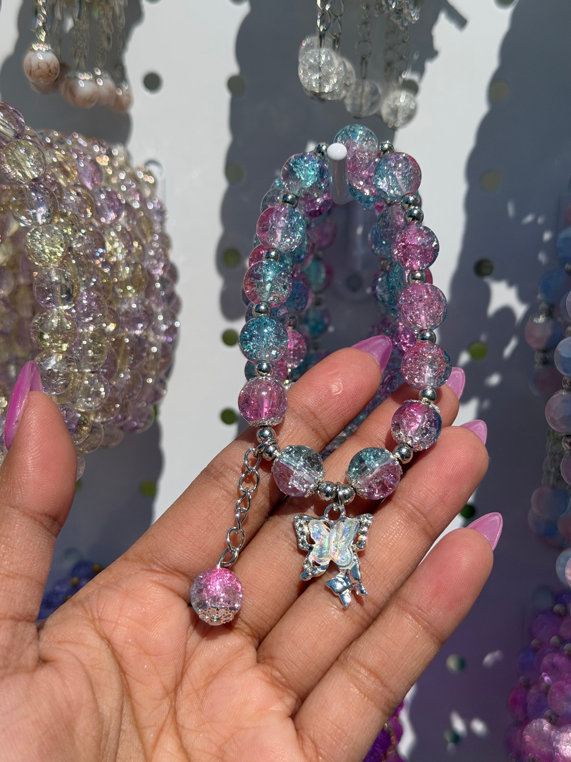 Lilac beaded bracelet with cracked pink and blue glass beads and a silver butterfly charm, held in a hand.