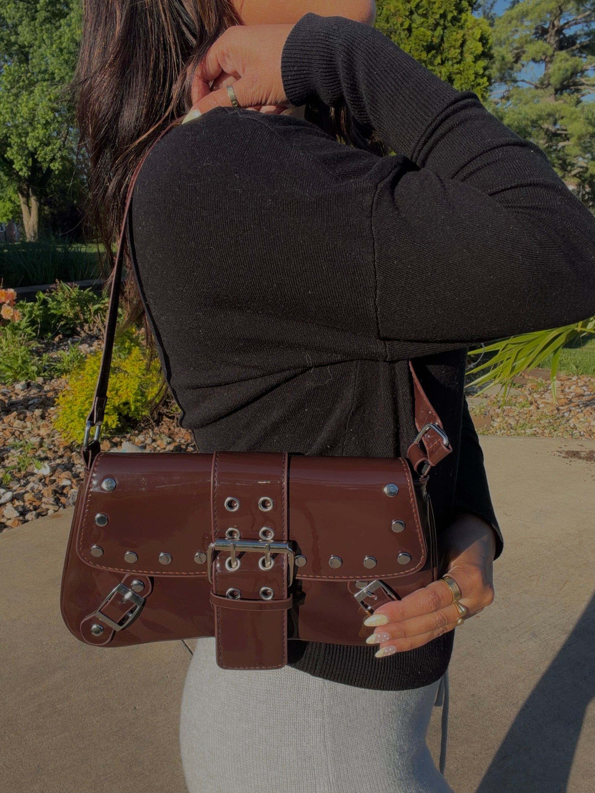 Shiny chocolate brown patent shoulder bag with silver studs and multiple buckle details.