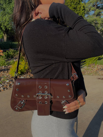 Shiny chocolate brown patent shoulder bag with silver studs and multiple buckle details.