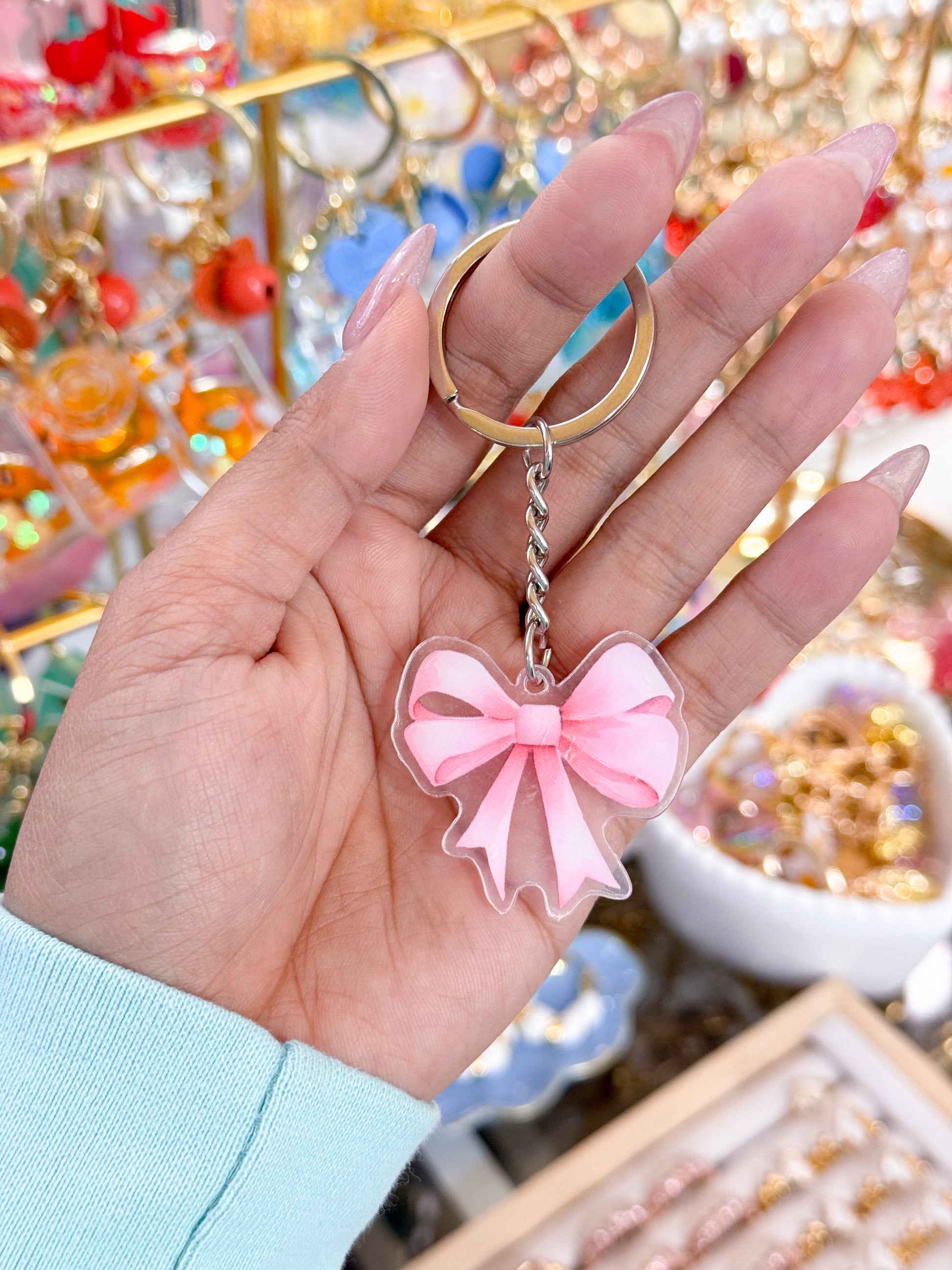 Pink bow keychain by Pretty In Plastic, held in a hand with acrylic nails.