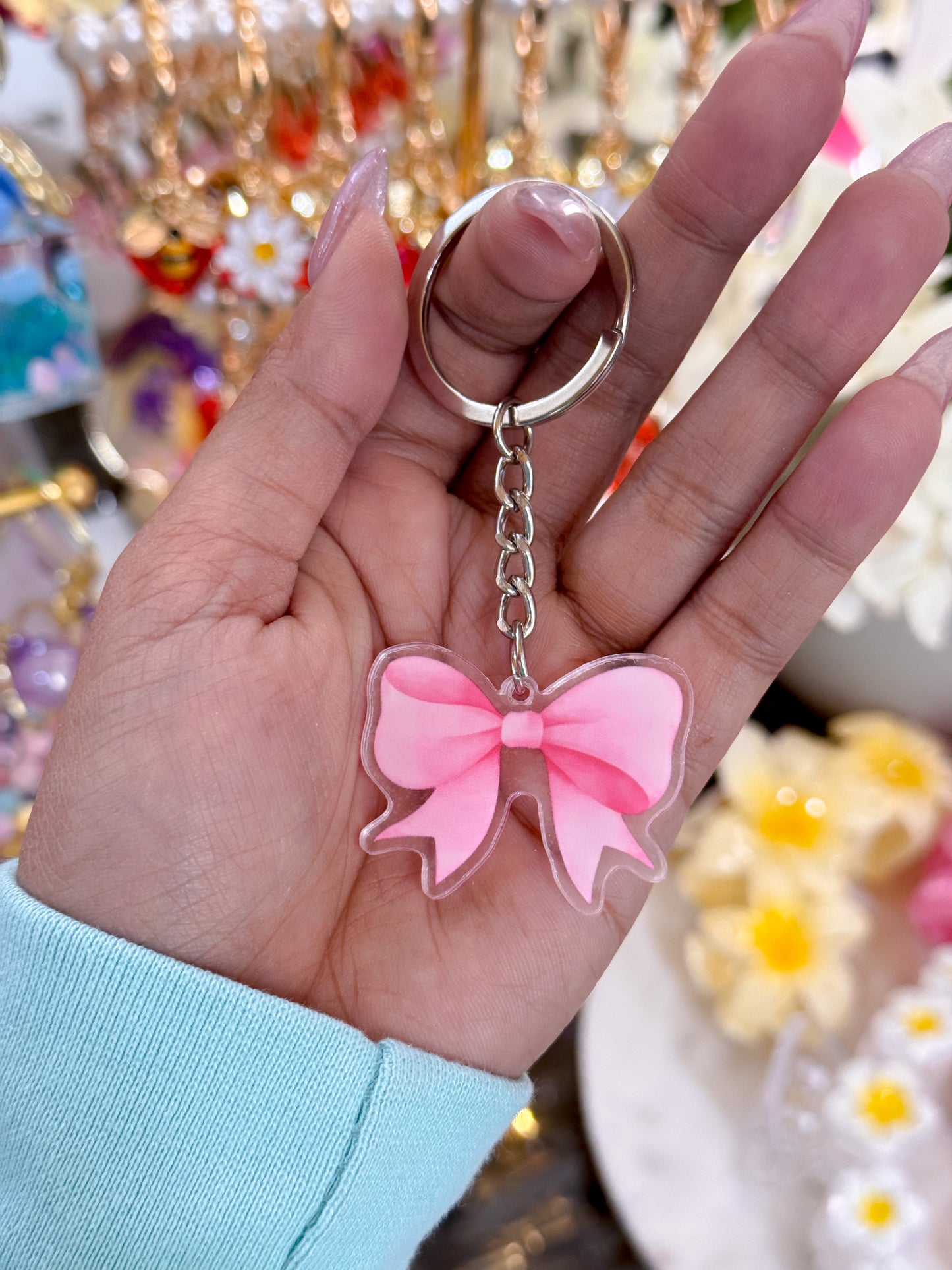 Pink bow keychain from 19 styles, held in a hand with long nails and a light blue sleeve.