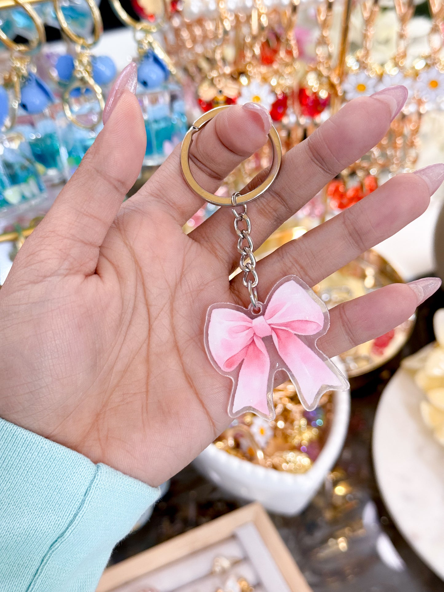 Pink bow keychain with silver keyring by vendor, held in hand with manicured nails.
