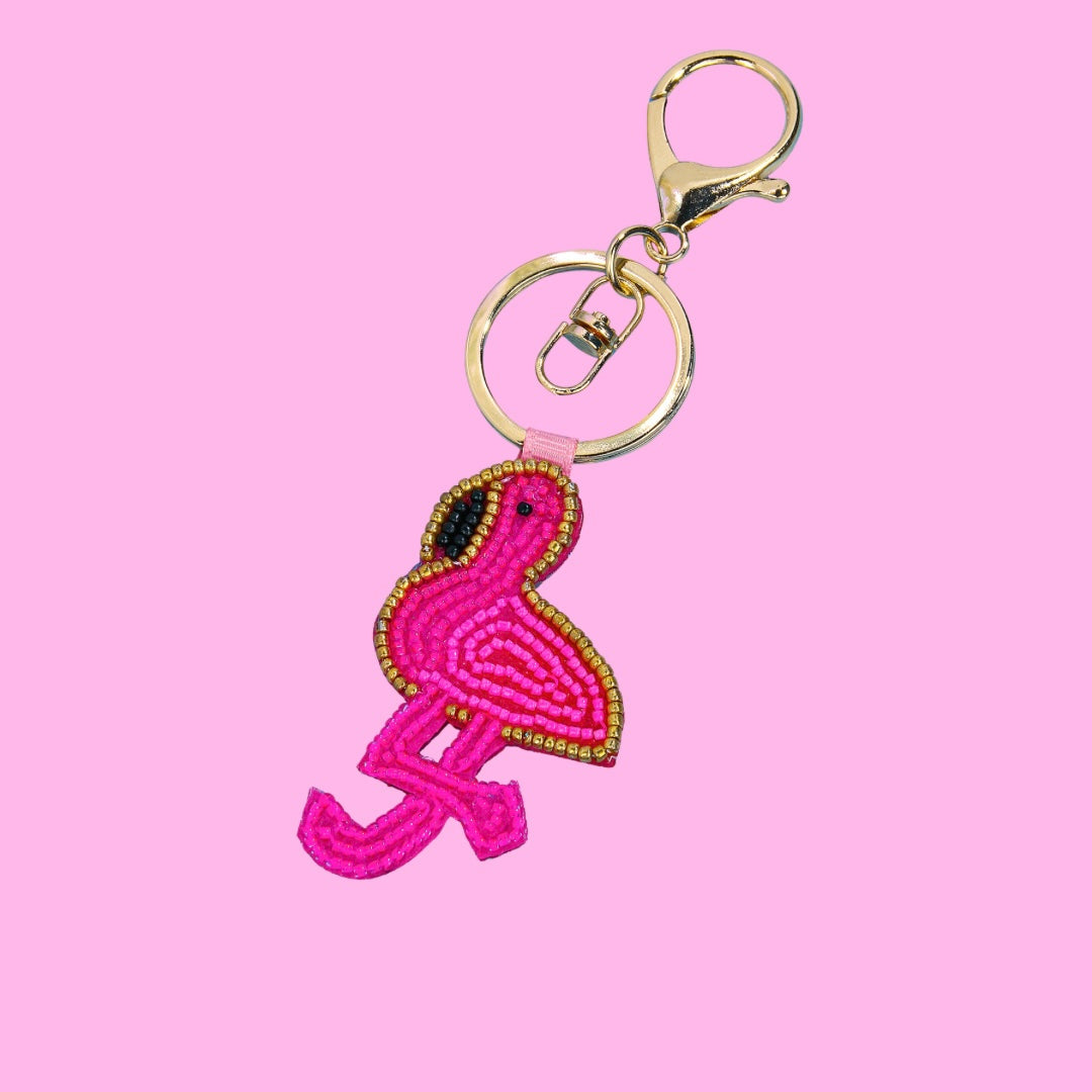 Pink beaded flamingo bag charm with a gold beaded outline and black bead details, attached to a gold-tone keychain.