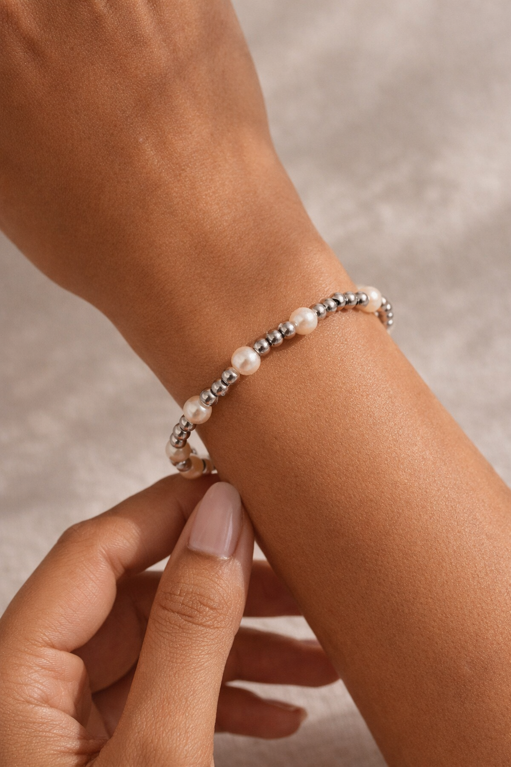 Pearl and silver beaded bracelet on a wrist, gently touched by a hand.