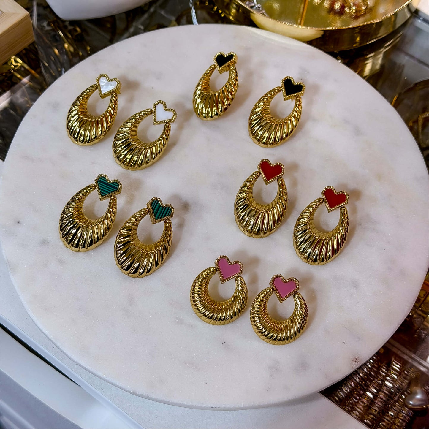Featuring a unique ribbed texture and a classic doorknocker silhouette, these statement earrings are designed to turn heads. The focal point is an attached heart charm filled with vibrant, smooth enamel in pink, black, green, white, and red.