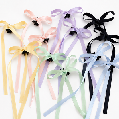 Set of bow mini hair clips with long satin ribbons in pastel yellow, pink, green, lavender, blue, and black, scattered on white.